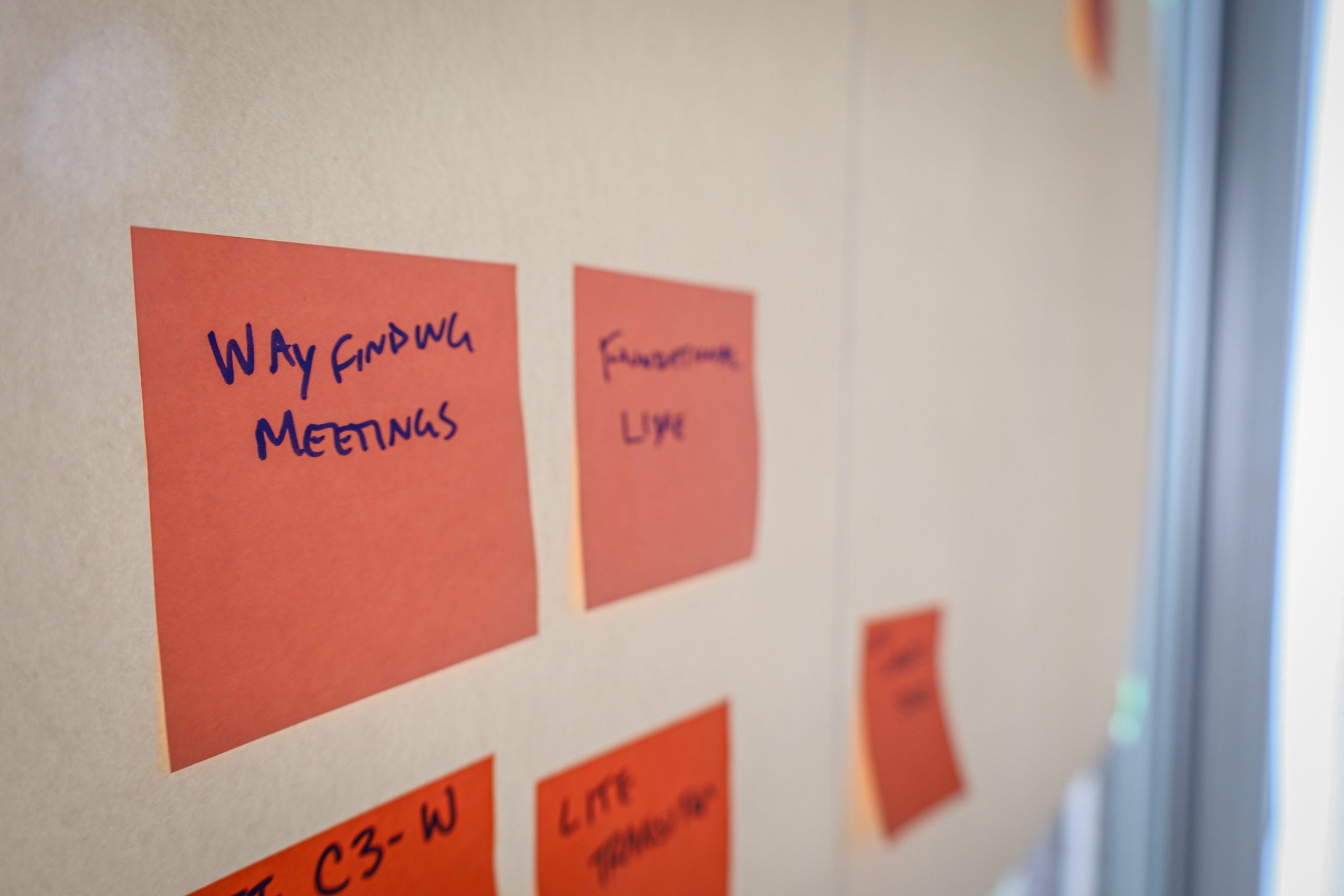 Brainstorm Notes Pink post-it notes on a white board. The note in focus reads "way finding meetings"